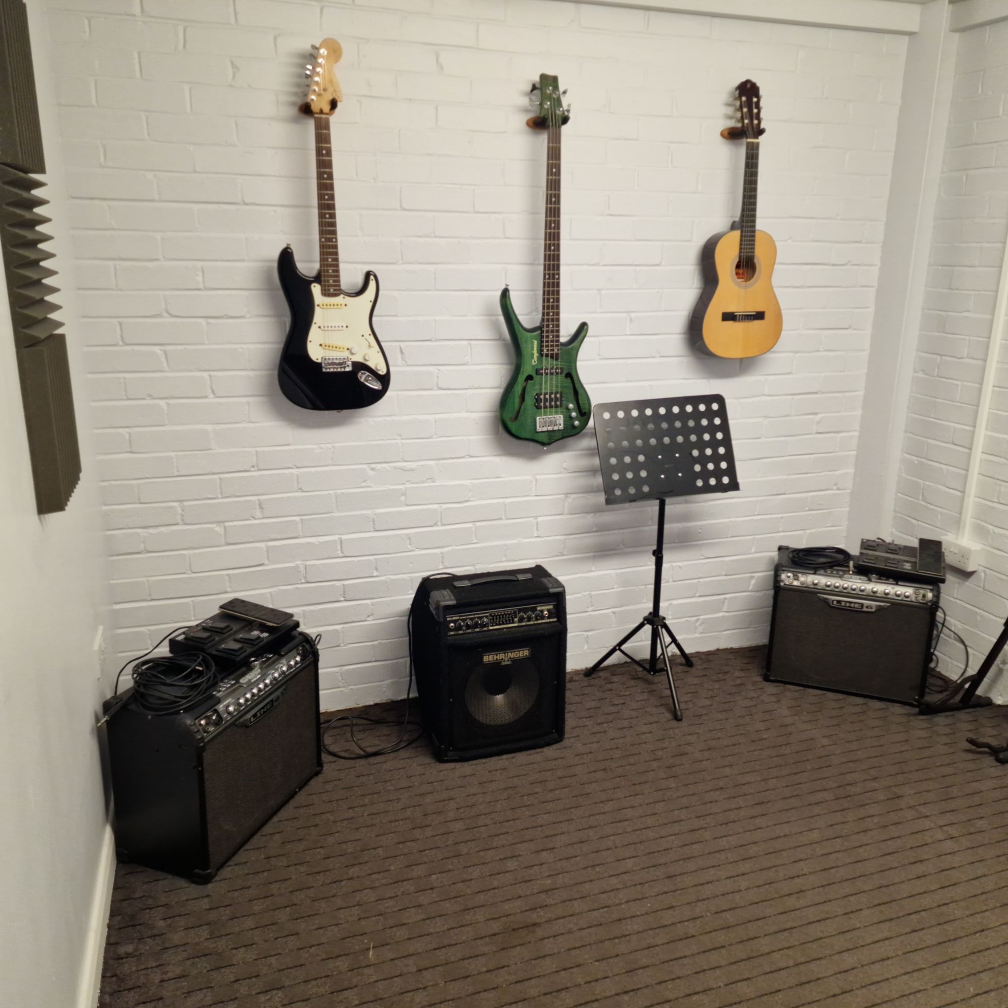A teaching room with an electric guitar, a bass guitar and a classical guitar on the wall above three amps