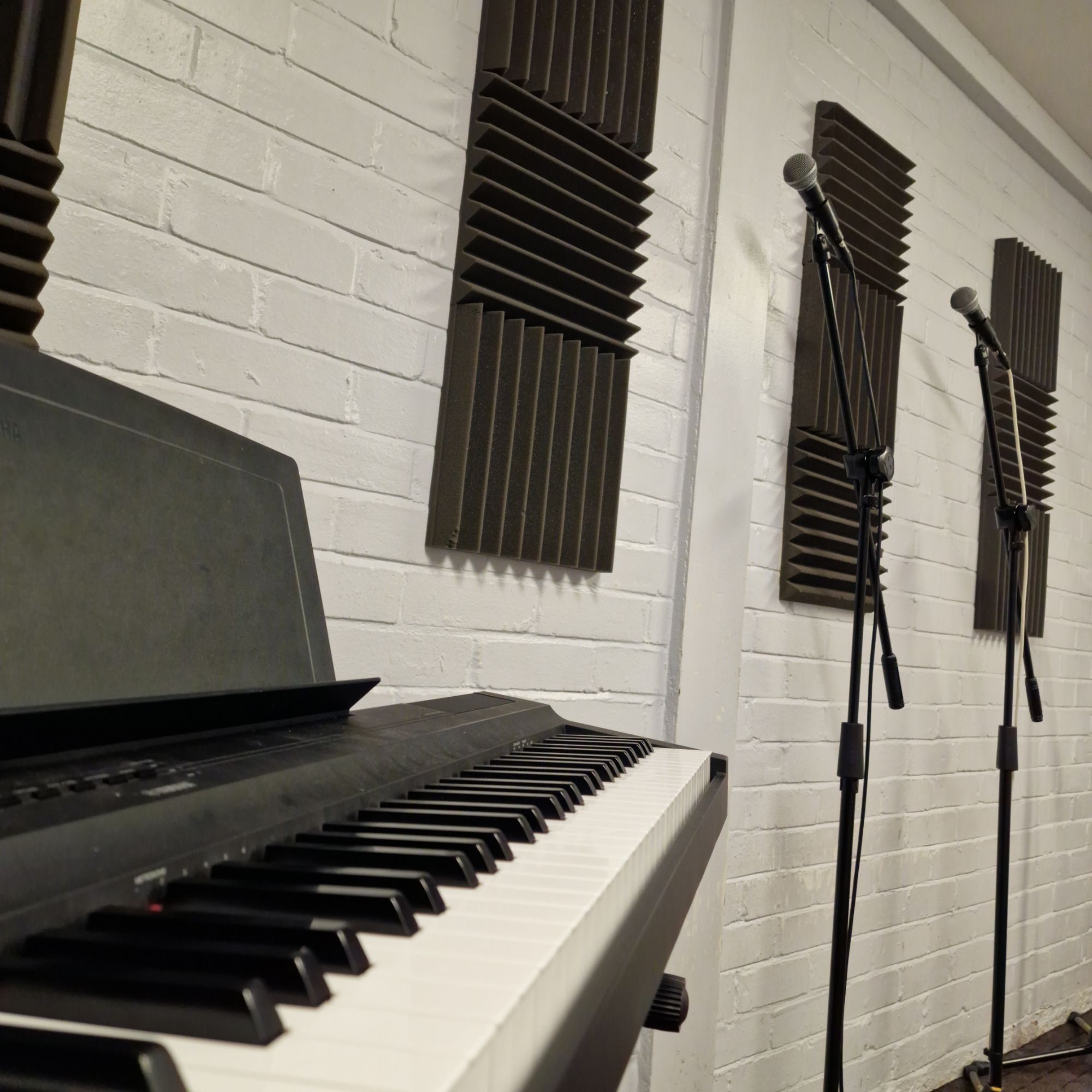A Yamaha keyboard and two microphones on stands in a teaching room with acoustic panels