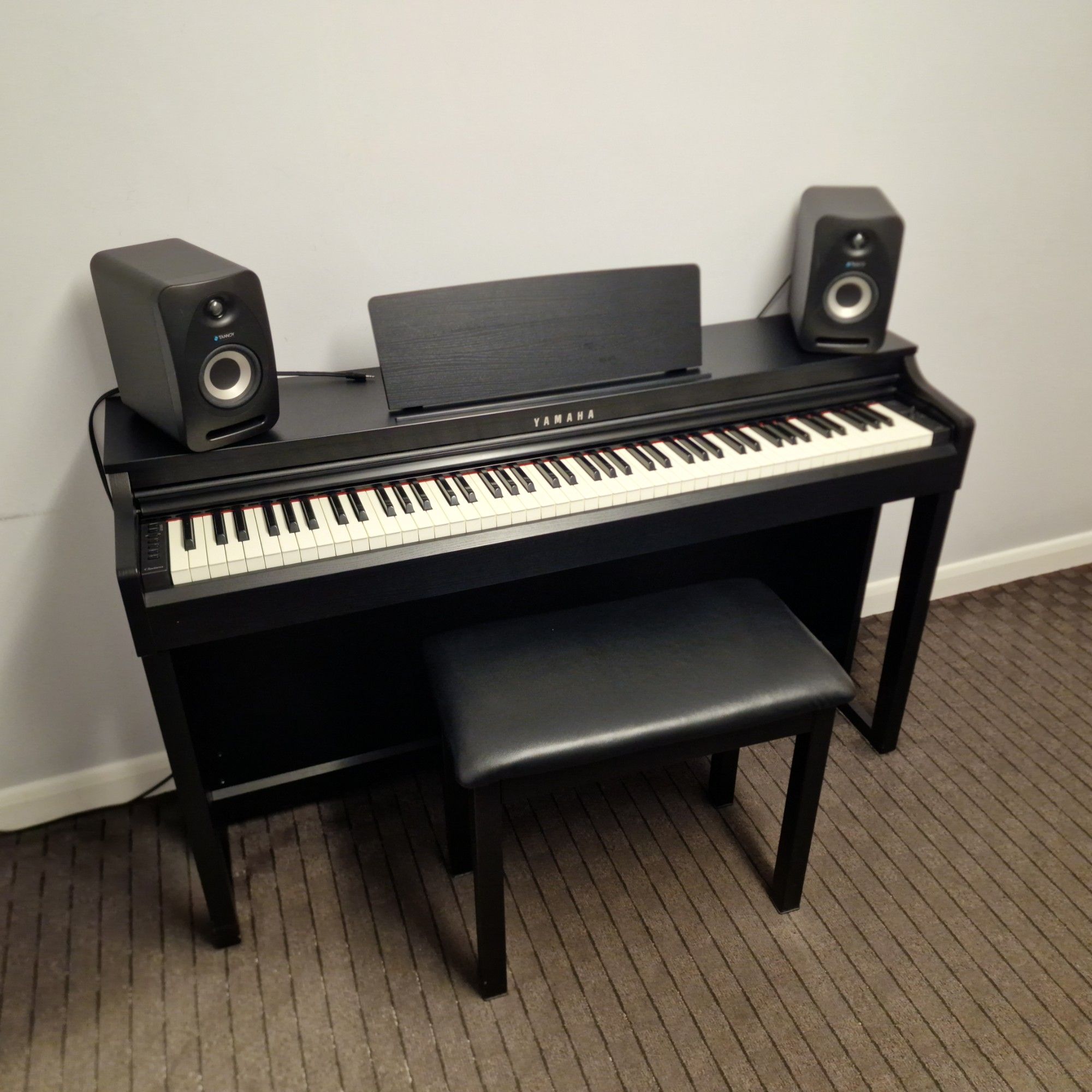 A Yamaha digital piano with a stool and studio speakers in a teaching room